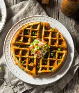 Image of Cheesy Cornmeal Waffles on a plate with sour cream and bacon topping