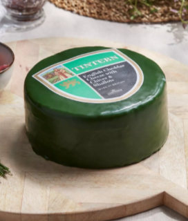 Photo of Somerdale Tintern Cheddar with green wax wrapper on a wooden cutting board. 