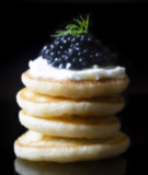 Photo of Tsar Nicoulai Caviar on a stack of blini against a black background