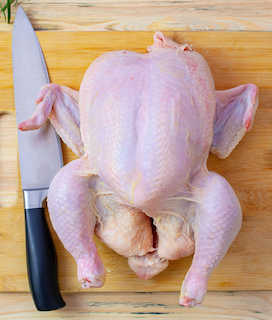 Photo of a whole, raw chicken on a cutting board for How to Cut Up a Whole Chicken