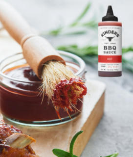 Kinder's Hot Barbecue Sauce on a table with a brush and ribs