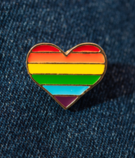 Photo of an enamel rainbow heart pin on denim for Oakland Pride