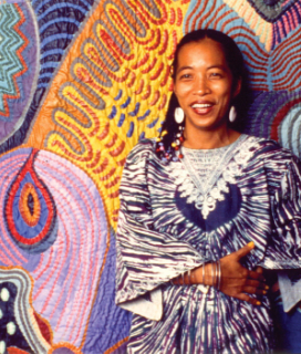 Portrait of Pacita Abad in front of one of her colorful quilts
