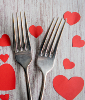 Photo of two forks on a table surrounded by cut-out hearts for A Cozy Valentines Dinner